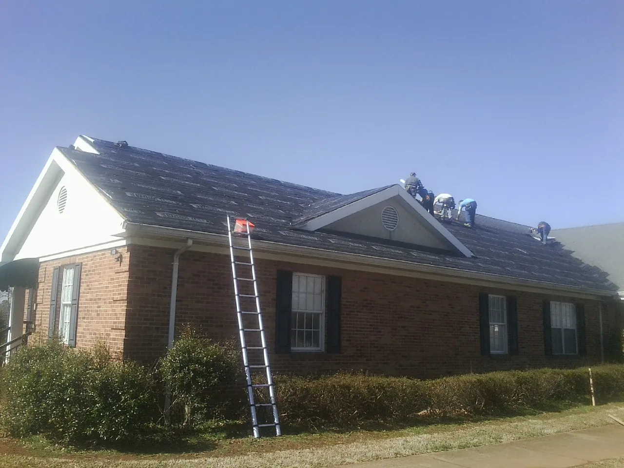 Crew tearing shingles off a brick ranch roof with a ladder set — Metal Roof Repair work by our crew in Cochranville