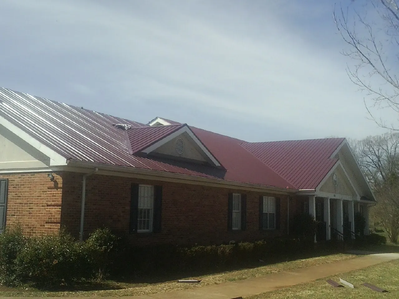 Red metal roof with gabled entries on a long brick building, from a Hail Damage Roof Repair job in Cochranville