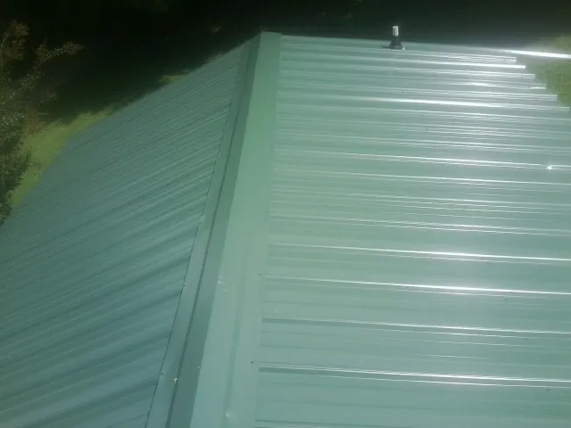 New green metal panels meeting at the ridge of a roof — Flat Roof Repair work by our crew in Cochranville
