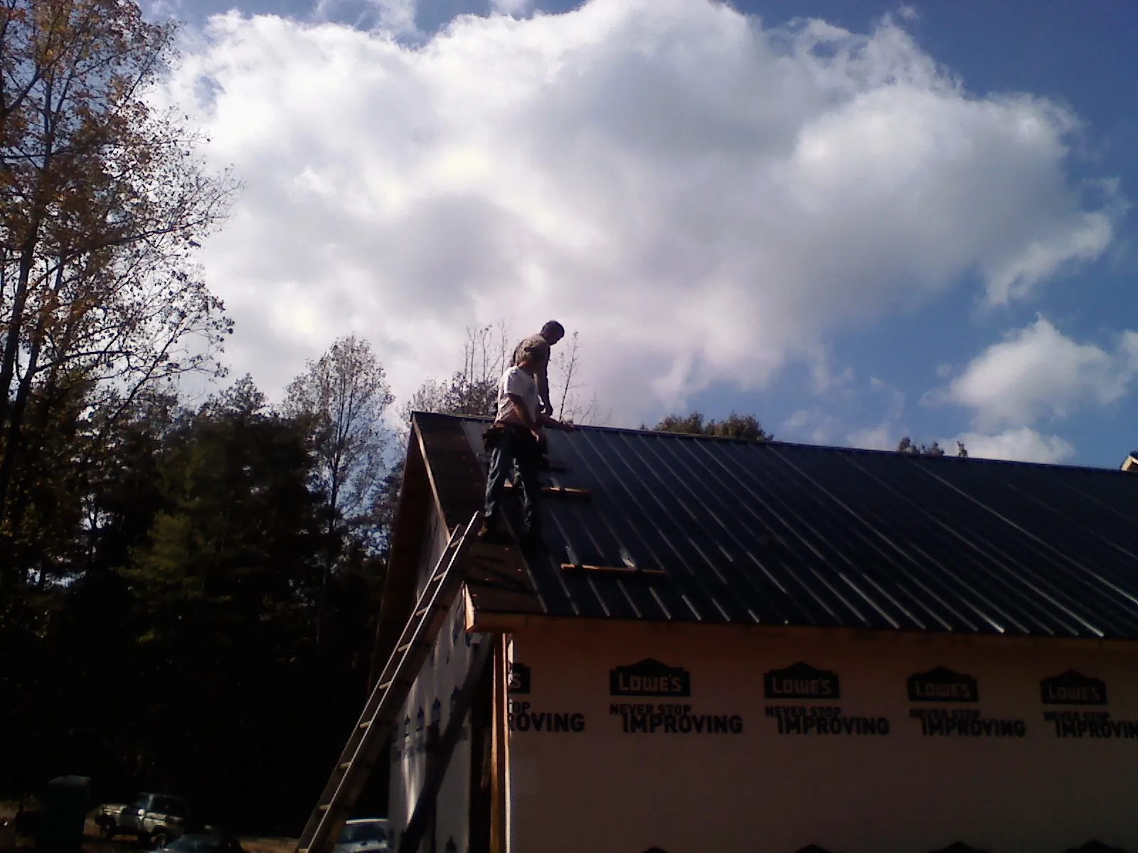 Roofer fastening dark metal panels high against a cloudy sky, from a Roof Inspection job in Cochranville