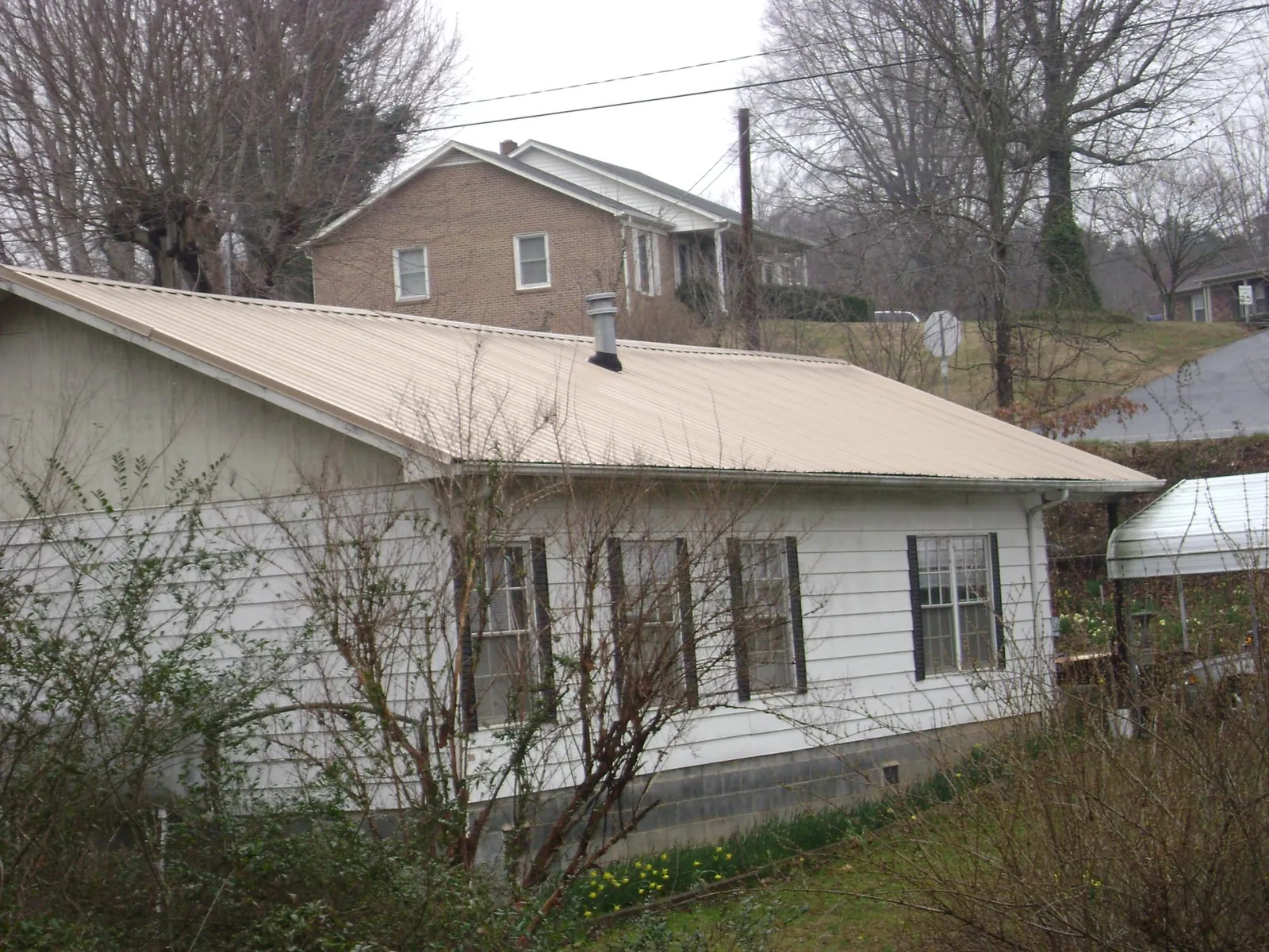 Tan metal roof on a white sided house set into a hillside — Commercial Roofing by Roofing Brothers in Cochranville